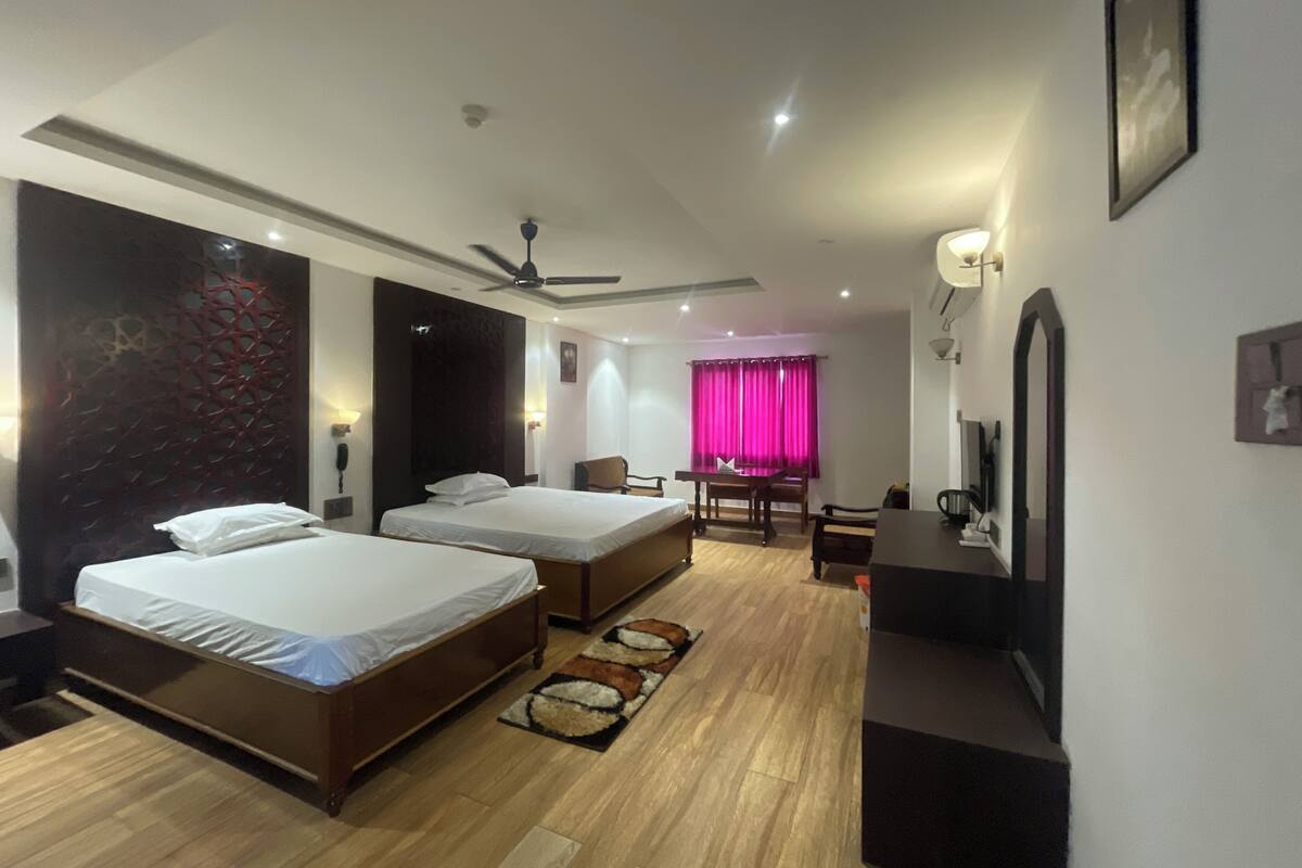 Une chambre d’hôtel avec deux lits, un bureau, une chaise, une télévision et un ventilateur de plafond.
