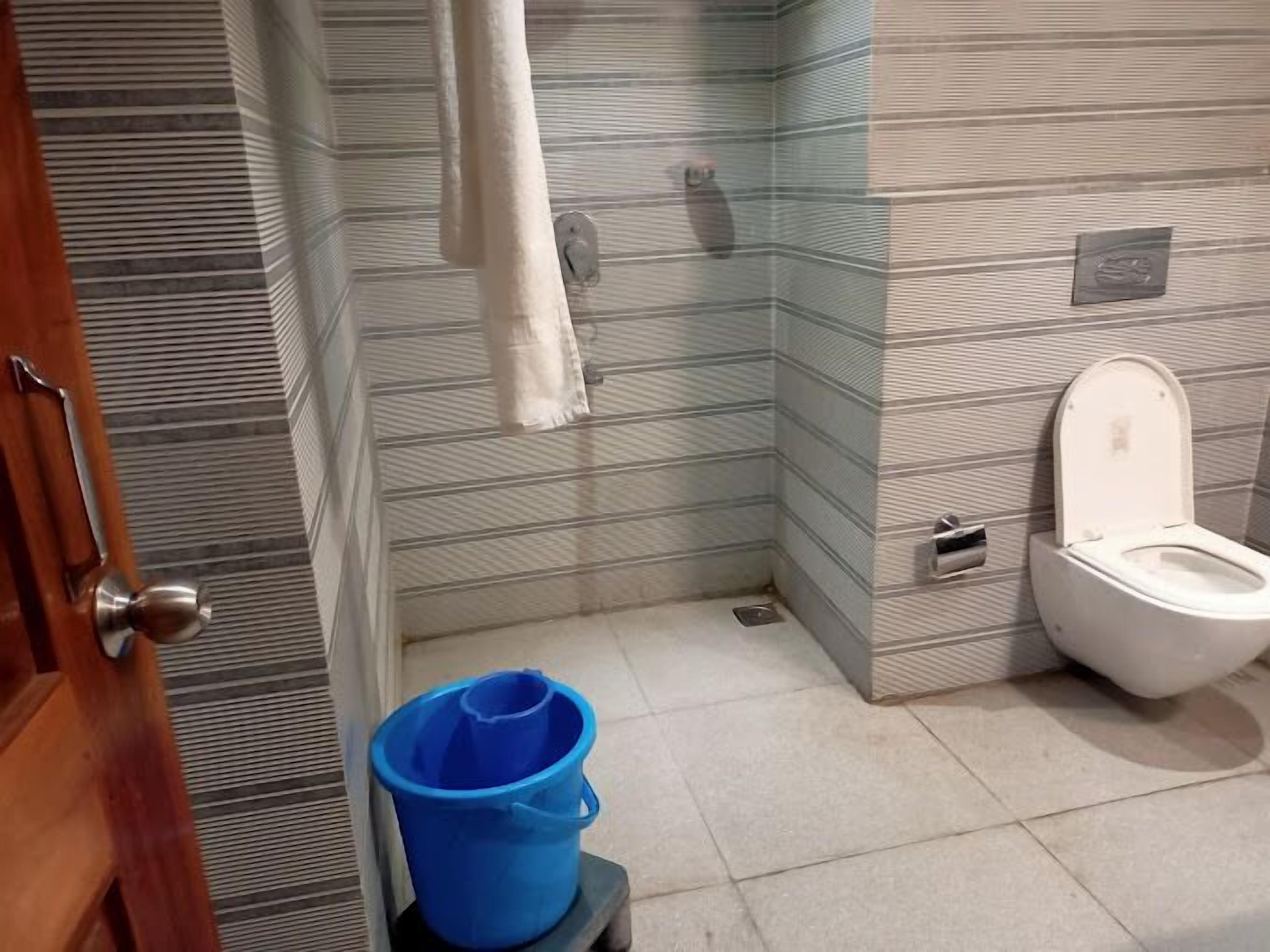 Un baño con paredes a rayas, un inodoro blanco, un cubo azul y una toalla colgada en la pared.