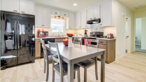Una cocina moderna con armarios blancos, electrodomésticos de acero inoxidable y un comedor con mesa y sillas.