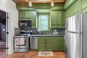 A kitchen with green cabinets, stainless steel appliances, and a tiled backsplash.