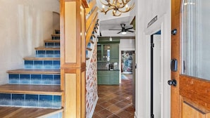Una escalera con escalones de madera y un candelabro, que conduce a una cocina con armarios verdes y piso de baldosas.