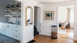 Une cuisine moderne avec des meubles blancs, un évier encastré et un crédence décorée. Un grand miroir est placé au-dessus de l’évier et un tableau encadré orne le mur.