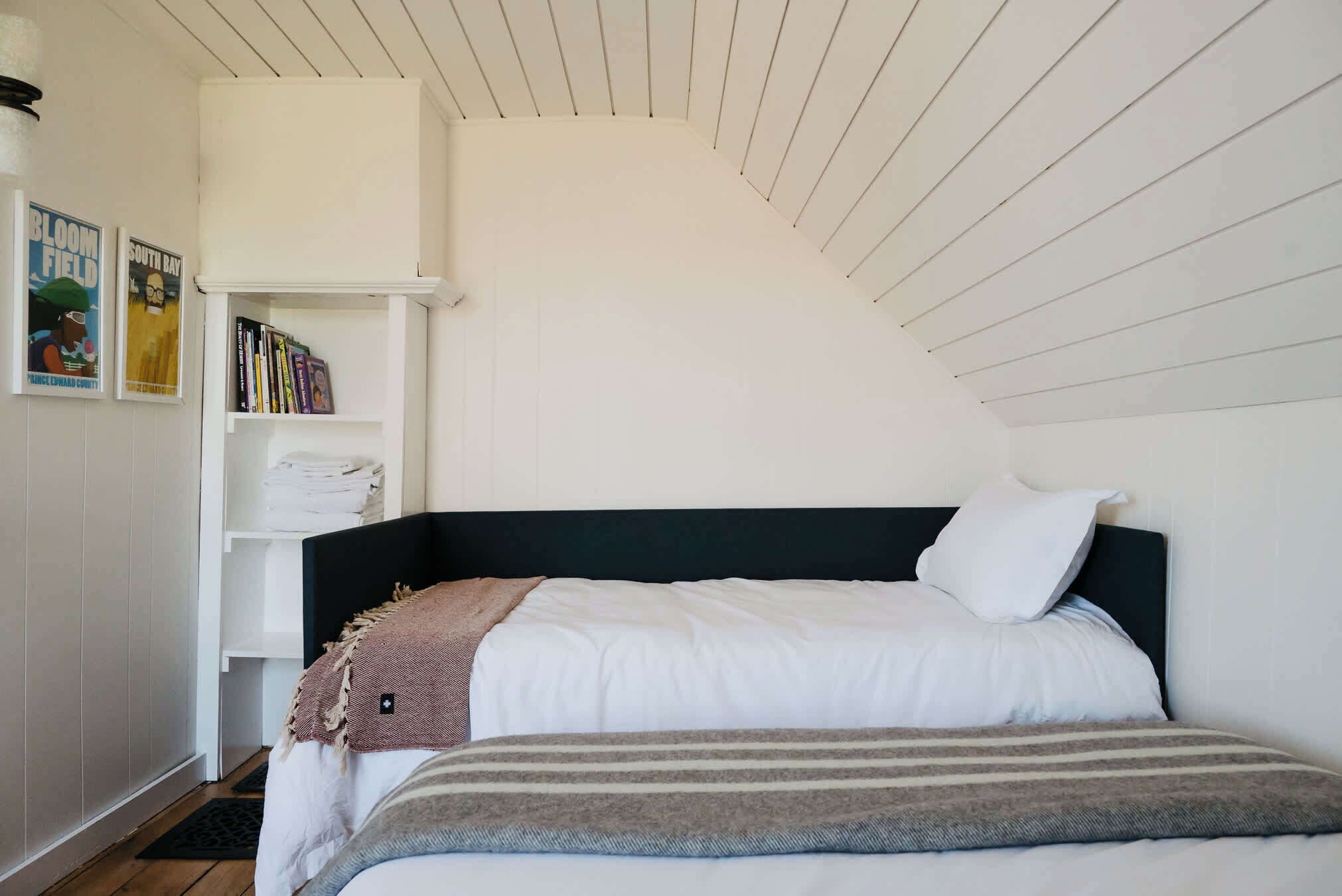 Een slaapkamer met een bed, een boekenkast en een schuine kap.
