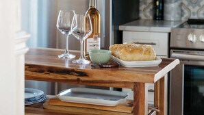 Une cuisine avec une table en bois, deux verres à vin, une bouteille de vin, une miche de pain et un bol.