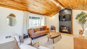 A living room with a wooden ceiling, a fireplace, a sofa, and a coffee table. - Modern Oregon Cottage w/ Hot Tub: Walk to Beach! (Cloverdale)