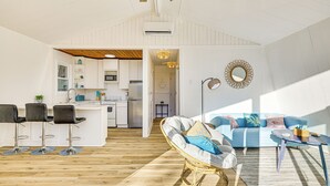 Et moderne køkken med hvide skabe, en central ø og et spiseområde med en blå sofa og fletstole.