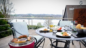 Un espace repas équipé d’un barbecue, d’une table, de chaises et offrant une vue sur un plan d’eau.