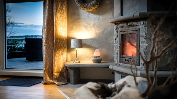Une pièce chaleureuse avec une cheminée en pierre, une lampe et une vue sur un paysage enneigé.