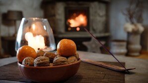 Un bol rempli d’oranges et de noix, posé sur un tapis, avec une cheminée en arrière-plan.