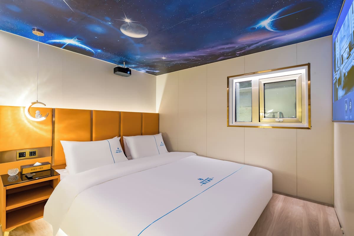 Een hotelkamer met een bed, nachtkastje en een plafond waarop een ruimte thema muurschildering is aangebracht.