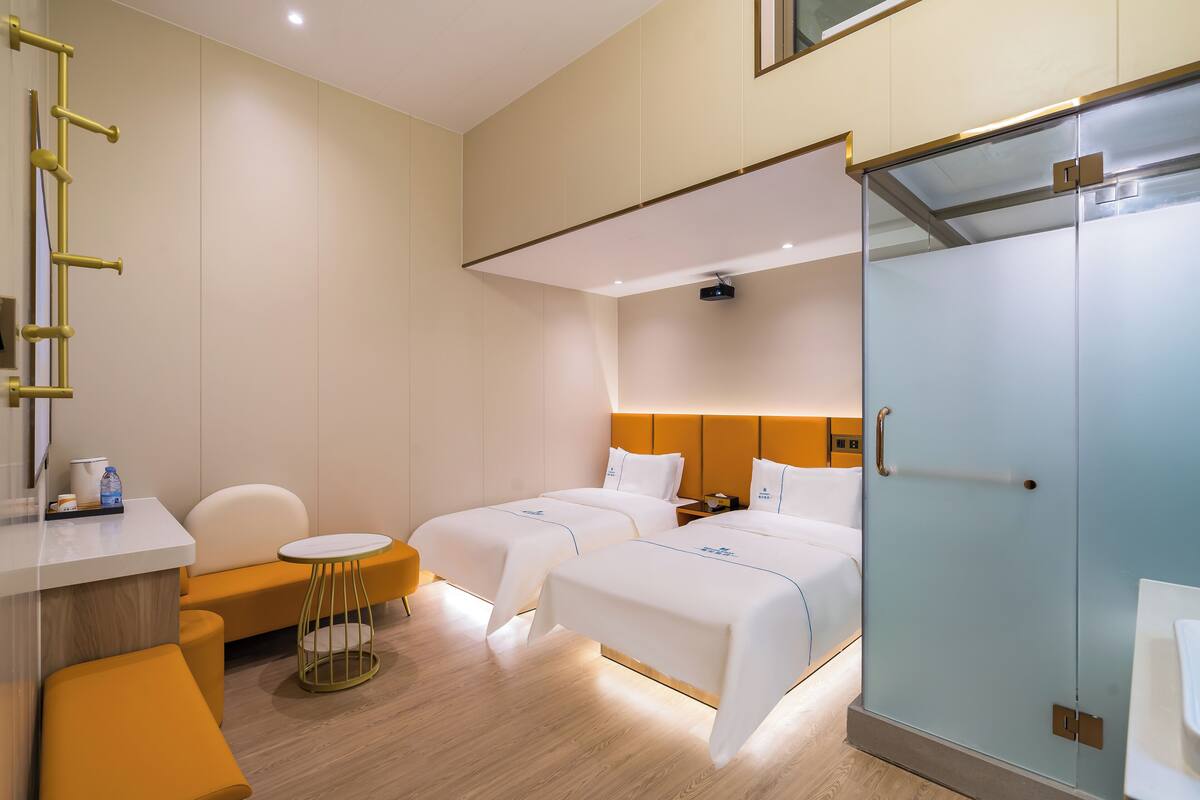Een hotelkamer met twee bedden, een kleine ronde tafel, een stoel, een kledingkast en een bureau met een spiegel en een lamp.