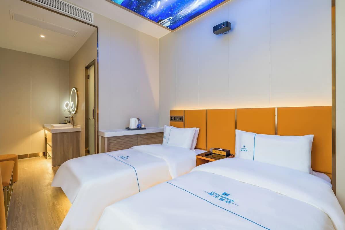 Een hotelkamer met twee bedden, een kaptafel met spiegel, een klein wastafeltje en een projector in het plafond.