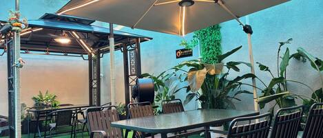 An outdoor patio area with a table and chairs, a large umbrella, artificial grass, and potted plants.