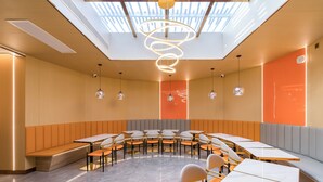 Un comedor moderno con mesas redondas y bancos, una lámpara espiral en el centro, y un tragaluz arriba.