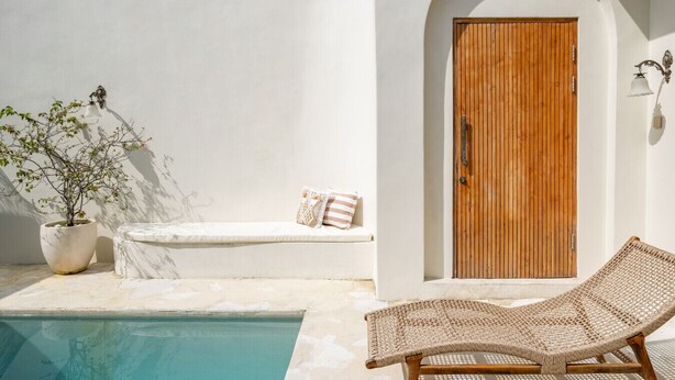 A poolside area with a wooden door, a lounge chair, a bench with cushions, and a potted plant. - Luxe Stunning 3BR Villa in Canggu, 8 mins to beach (Canggu)