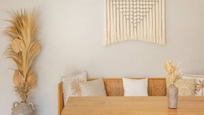 A room with a wooden dining table, wicker sofa with patterned cushions, a macrame wall hanging, and a vase with dried plants. - Luxe Stunning 3BR Villa in Canggu, 8 mins to beach (Canggu)