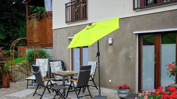 Een terras met buitenmeubilair, een felgele parasol en een gebouw met een balkon en schuifdeuren.