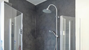 A modern shower with a handheld showerhead and a wall-mounted rain showerhead, set against dark grey tiles.