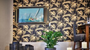 A room with a wall-mounted TV, a framed picture, a potted plant, and a black leather chair.
