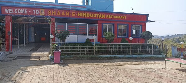 Un restaurante llamado Shaan-E-Hindustan con fachada roja y azul, una entrada acogedora y un camino pavimentado en su frente.