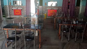 A restaurant with multiple tables and chairs, a counter with a menu, and a sign indicating it serves Shankari Hindustan cuisine. - Hindustan Hotel (Gobindpur)
