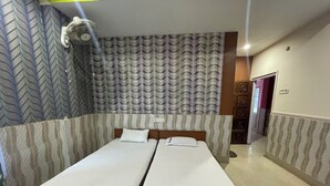A room with two single beds, a ceiling fan, patterned wallpaper, and a hallway with a door.