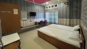A hotel room with a large bed, a desk, a chair, a TV, and patterned wallpaper.