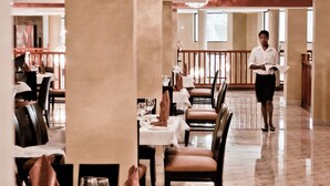 Un restaurante con mesas dispuestas para comer, un camarero caminando y una araña de cristal.