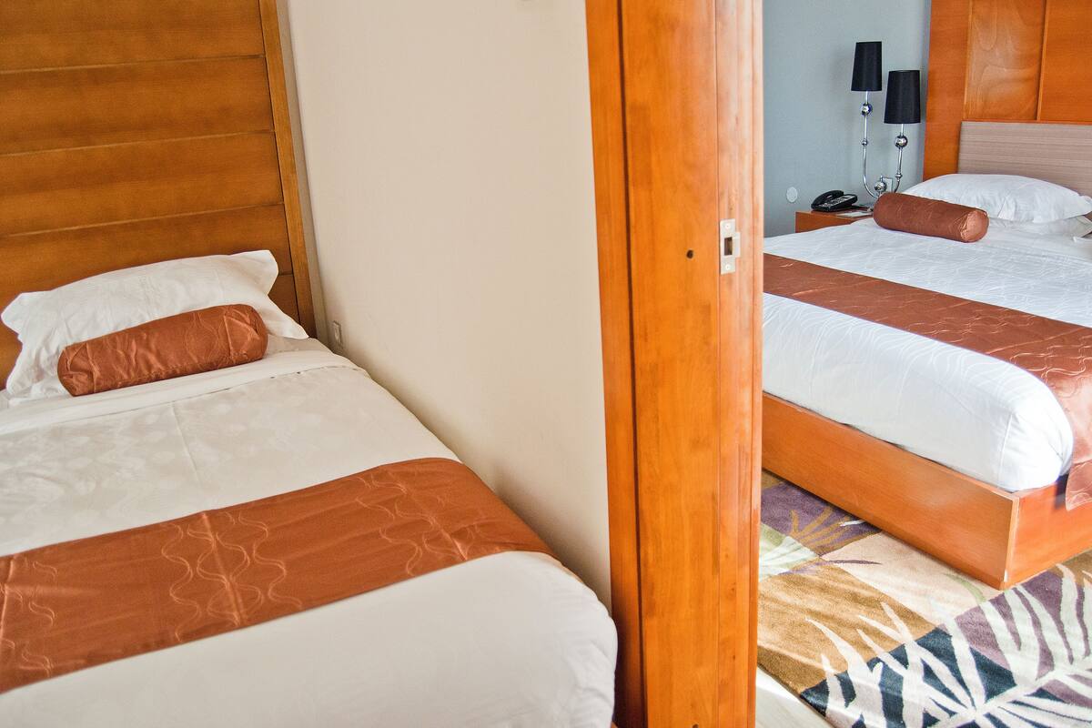 Two adjacent beds with wooden headboards, white linens, and brown decorative pillows.