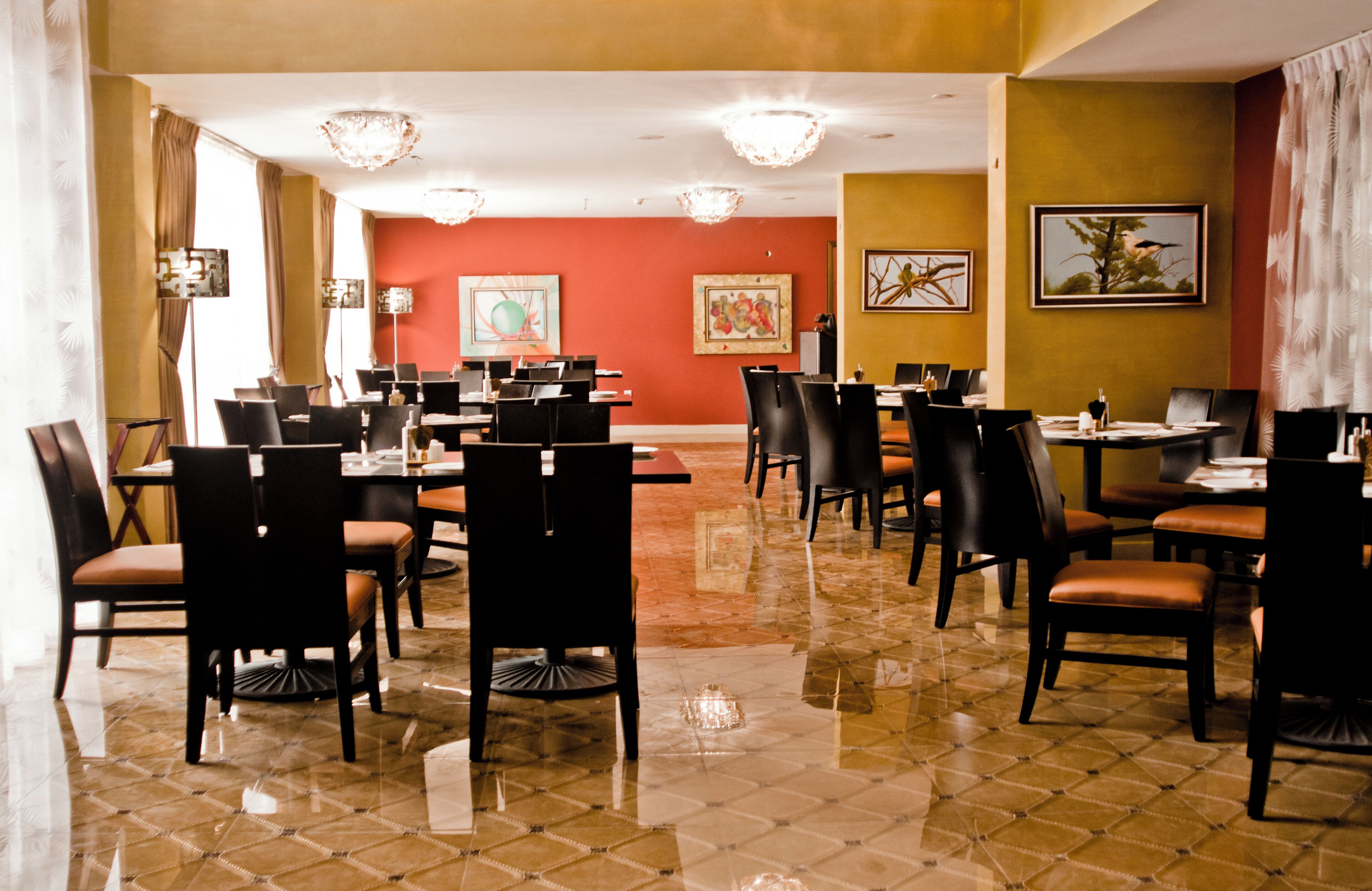 A spacious dining area with multiple tables and chairs, a polished floor, and artwork on the walls.