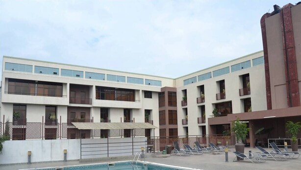 Un área de piscina con una pileta rectangular, sillas de descanso y un edificio de varios pisos con balcones y ventanas.