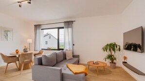 En moderne stue med sofa, spisebord, stole, et lille rundt bord og en potteplante.