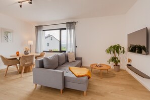 Ein modernes Wohnzimmer mit einer Couch, einem Esstisch, Stühlen, einem kleinen runden Tisch und einer Topfpflanze.