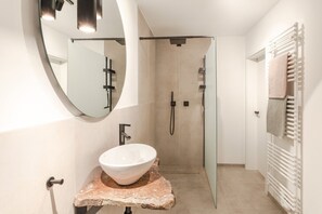 A modern bathroom with a round mirror, a white sink, a shower, and a towel rack.