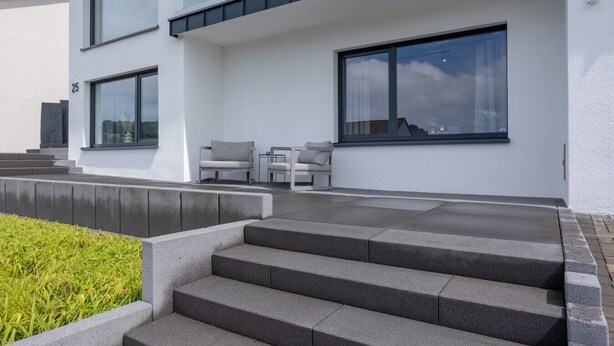 En moderne bygning med en trappe, der fører til en balkon, udendørs siddepladser og store vinduer.