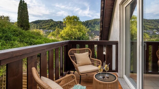 Un balcon agrémenté de meubles en osier, d’une table en verre et offrant une vue sur une zone boisée.