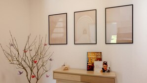 Un espace d’accueil agrémenté d’un vase rempli de branches et d’oiseaux colorés, une console en bois sur laquelle repose un livre intitulé « Intérieurs new-yorkais », et trois tableaux encadrés accrochés au mur.