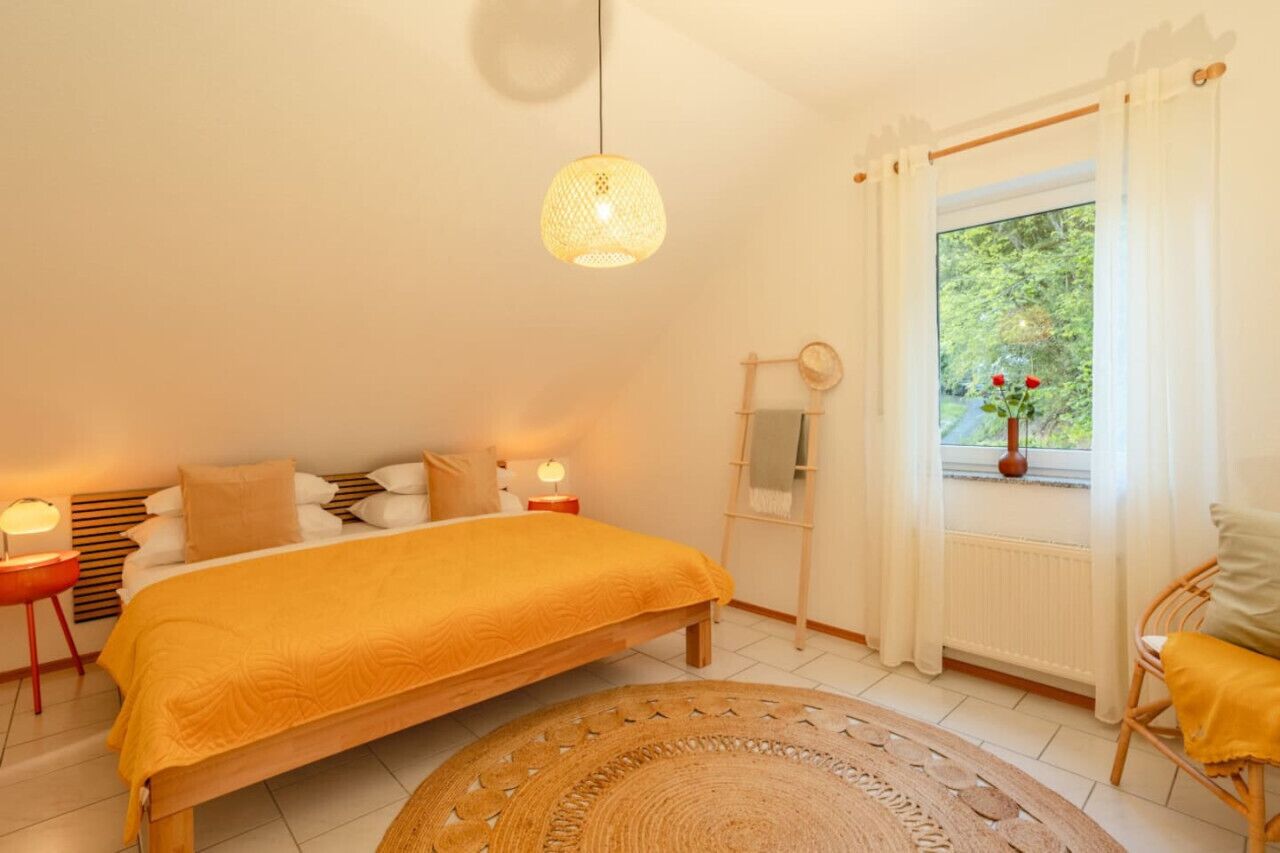 Une chambre à coucher avec un lit, des lampes de chevet, une fenêtre avec des rideaux et une vue sur la verdure à l’extérieur.