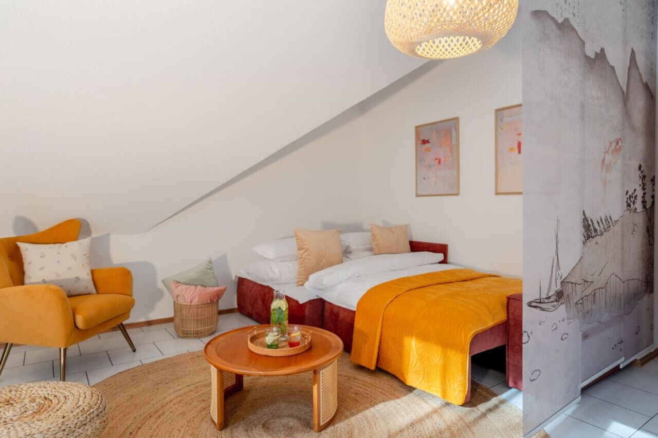 Une chambre confortable avec un lit, une chaise, une petite table et un mur décoré d’œuvres d’art.