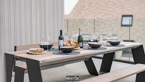 Mesa de jantar posta com pratos, tigelas, copos de vinho e uma garrafa, com um fundo arquitetônico moderno.
