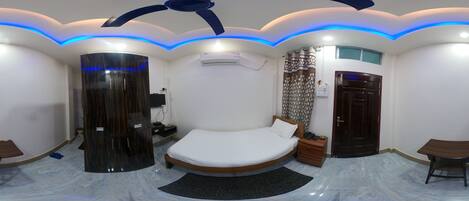 Un dormitorio moderno con una cama curvada, un pilar cilíndrico oscuro, una mesita de noche de madera e iluminación LED azul en el techo.