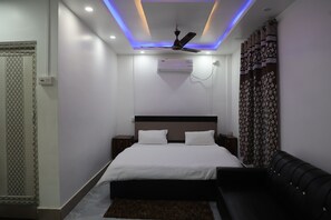 A modern bedroom with a bed, bedside tables, an air conditioning unit, a ceiling fan, and a decorative curtain. - Mayur Residency & Banquet (Dhemaji)