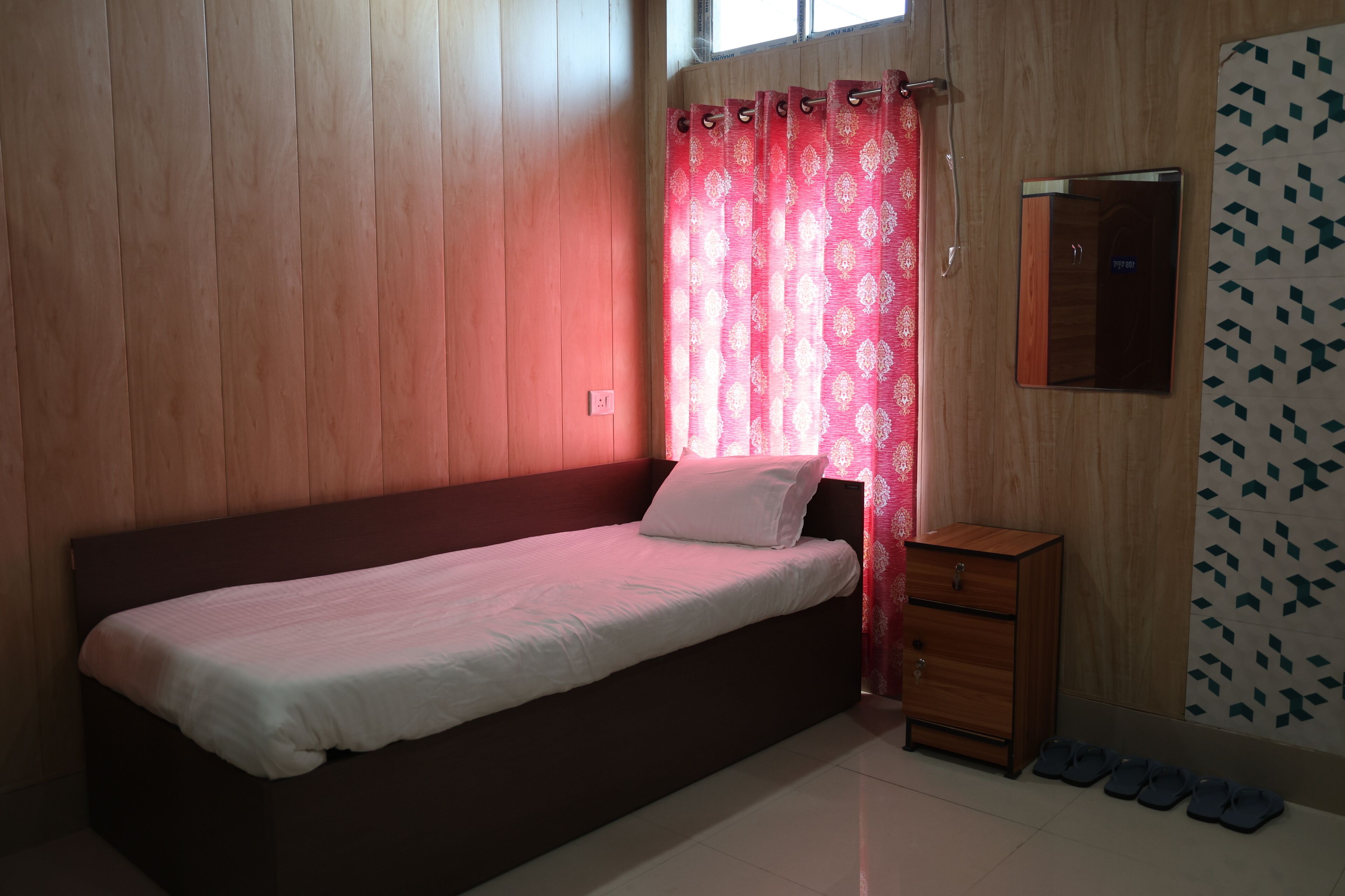 A small, single-bed room with a wooden headboard, a wooden nightstand, and a mirror on the wall.