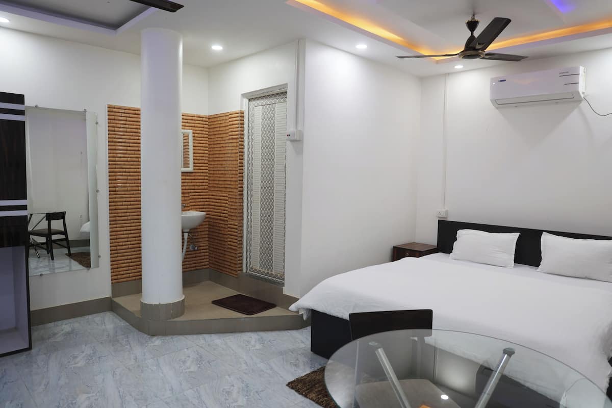 A modern hotel room with a bed, a glass table, a ceiling fan, and an air conditioning unit.