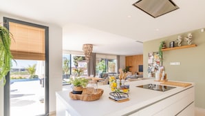 A modern kitchen with a large island, wooden sideboard, and a dining area with a view of the outdoors. - Casa Amorosa by Solidays - Moraira, Costa Blanca (Moraira)
