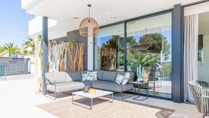 A modern outdoor living area with a gray sofa, a coffee table, and a wicker pendant light. - Casa Amorosa by Solidays - Moraira, Costa Blanca (Moraira)