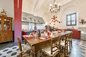 Comedor con una mesa de madera dispuesta para seis personas, rodeada de sillas de mimbre. Un candelabro cuelga del techo, y las paredes están decoradas con ollas y sartenes de cobre.