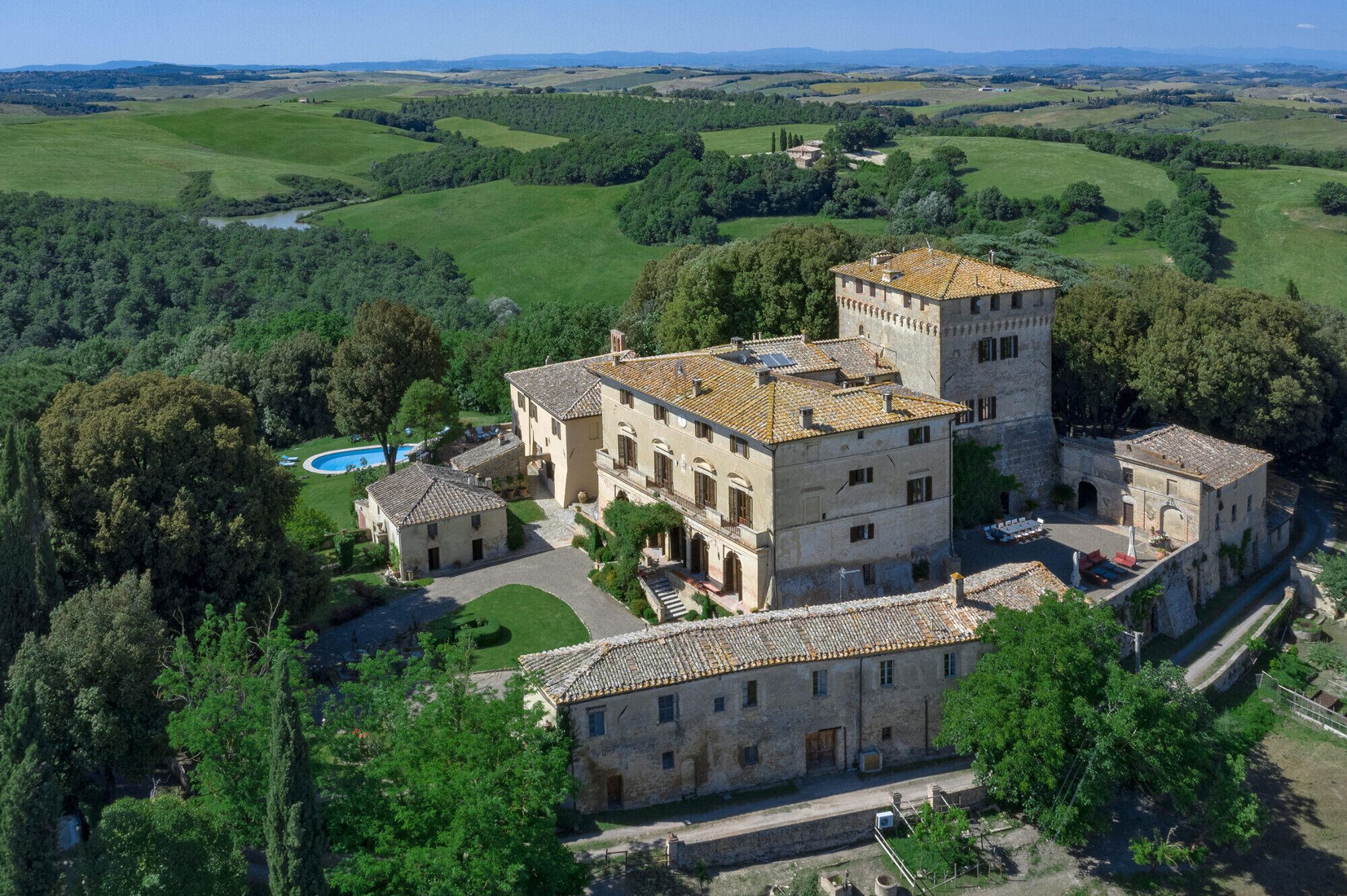A large, historic building with multiple structures, surrounded by lush greenery and a clear sky.