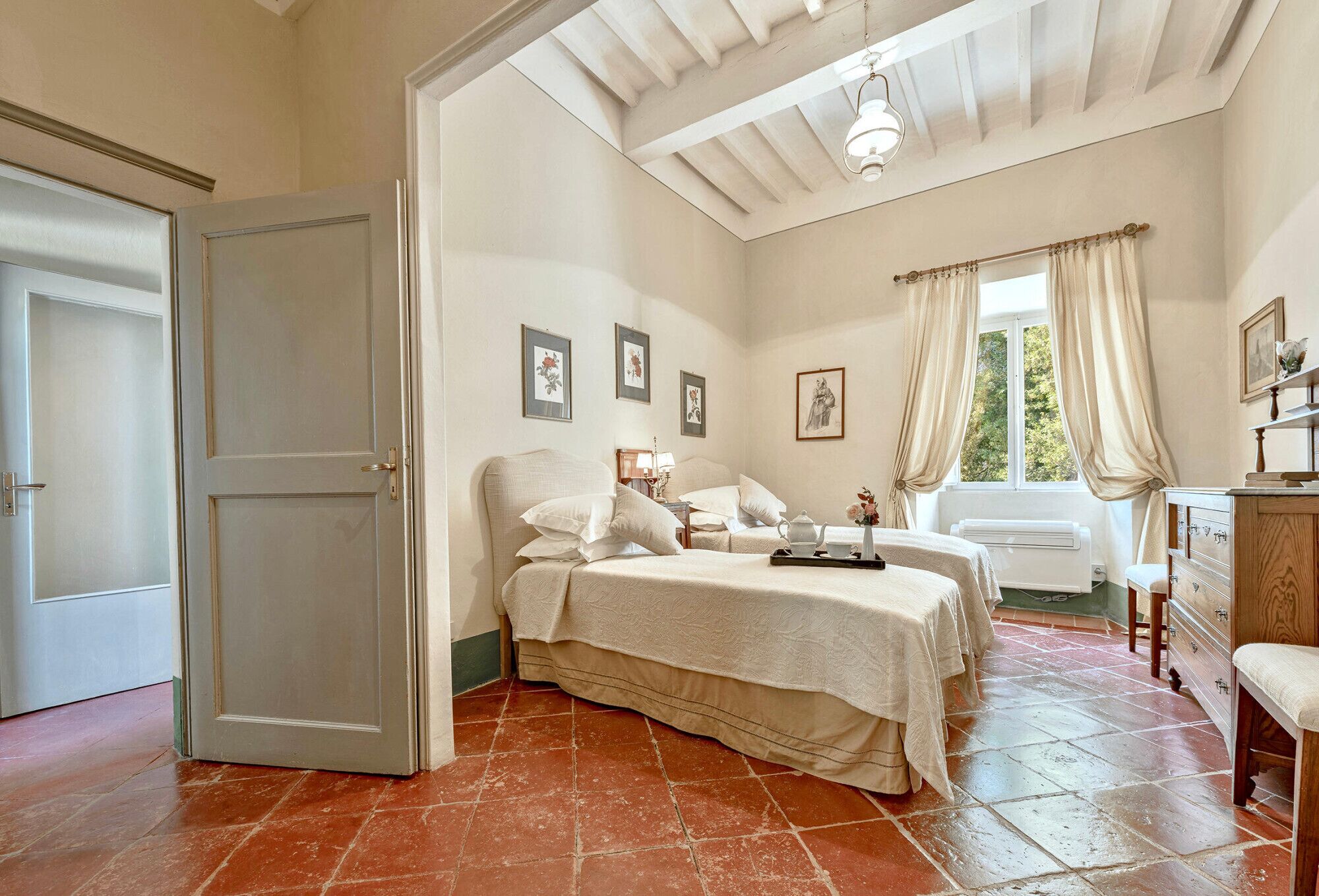 A bedroom with a large bed, a bedside table, a dresser, and a window with curtains.