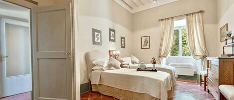 A bedroom with a large bed, a bedside table, a dresser, and a window with curtains.
